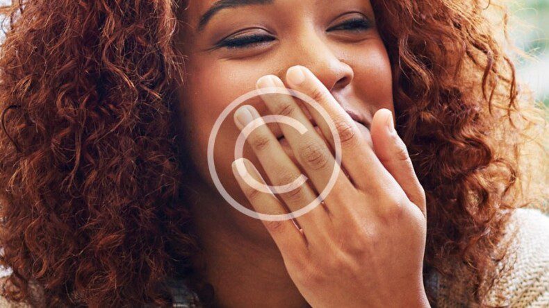 A woman with curly hair eating a hot dog.
