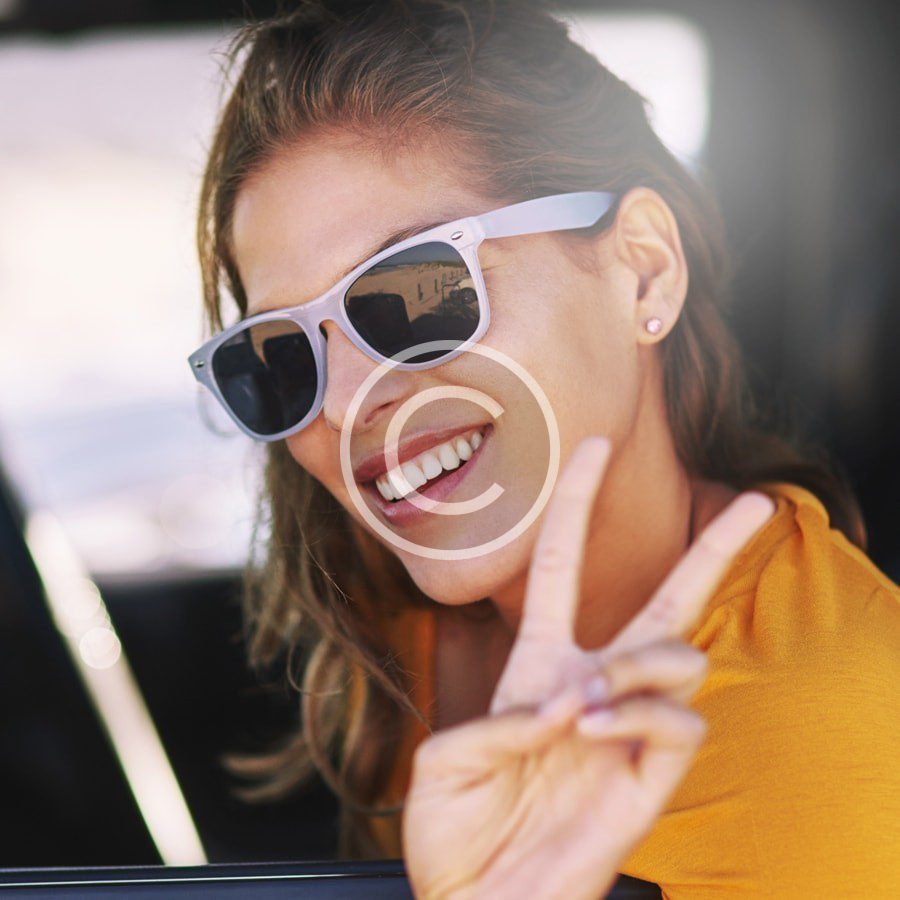 A woman wearing sunglasses and making a peace sign in a car.