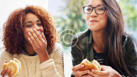 A woman is eating a burger and another woman is eating a sandwich.