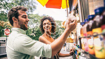 A man and woman standing next to a food truck.