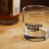 A WRS Rocks Glass on a table next to a bottle of whiskey.